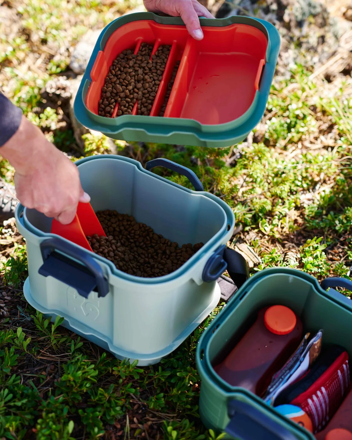 Scooping kibble by hand into Basecamp's open middle-tier food storage bucket.
